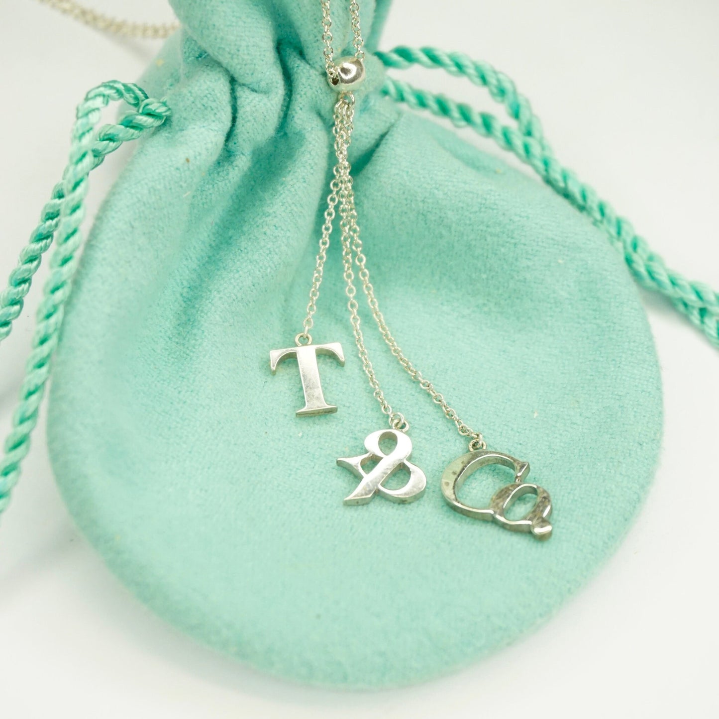 Vintage Tiffany & Co. sterling silver letter charm lariat necklace on mint green jewelry pouch, minimalist 925 silver chain jewelry.