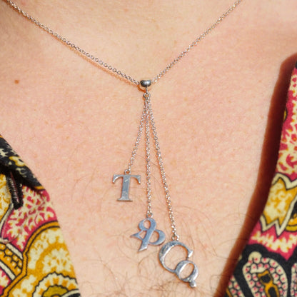 Vintage Tiffany & Co. sterling silver lariat necklace with T&CO letters pendant on a minimalist silver chain, worn over patterned clothing.