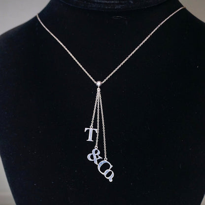 Vintage Tiffany & Co. sterling silver lariat necklace with T&CO letters pendant, minimalist 925 silver chain necklace on black display.