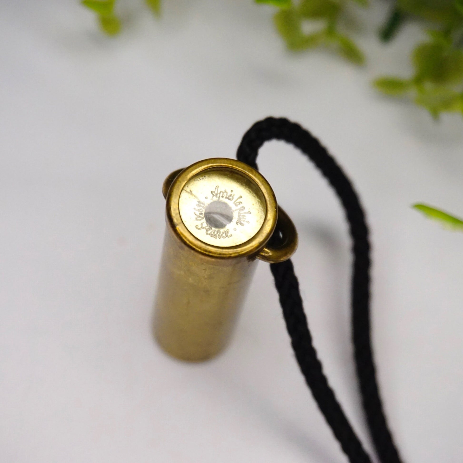 Vintage brass kaleidoscope pendant necklace made in France with black rope against a white background with green leaves