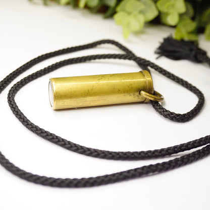 Vintage brass kaleidoscope pendant necklace with black rope, made in France, laying on white background with green leaves in soft focus, unique kaleidoscope jewelry