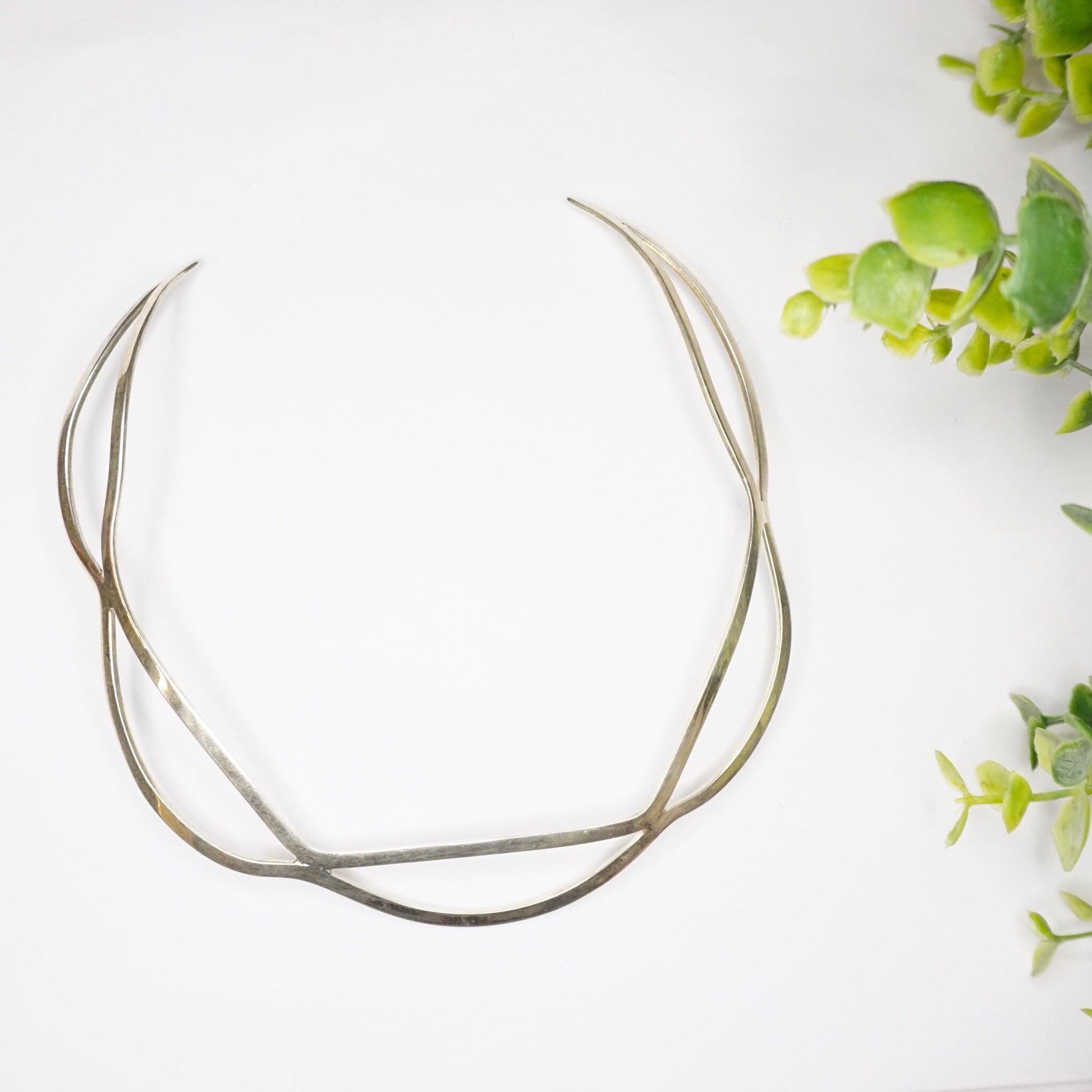 Vintage sterling silver cut out collar necklace from Mexico, 925 silver choker with wavy modern minimalist design, displayed with green plant leaves on white background.