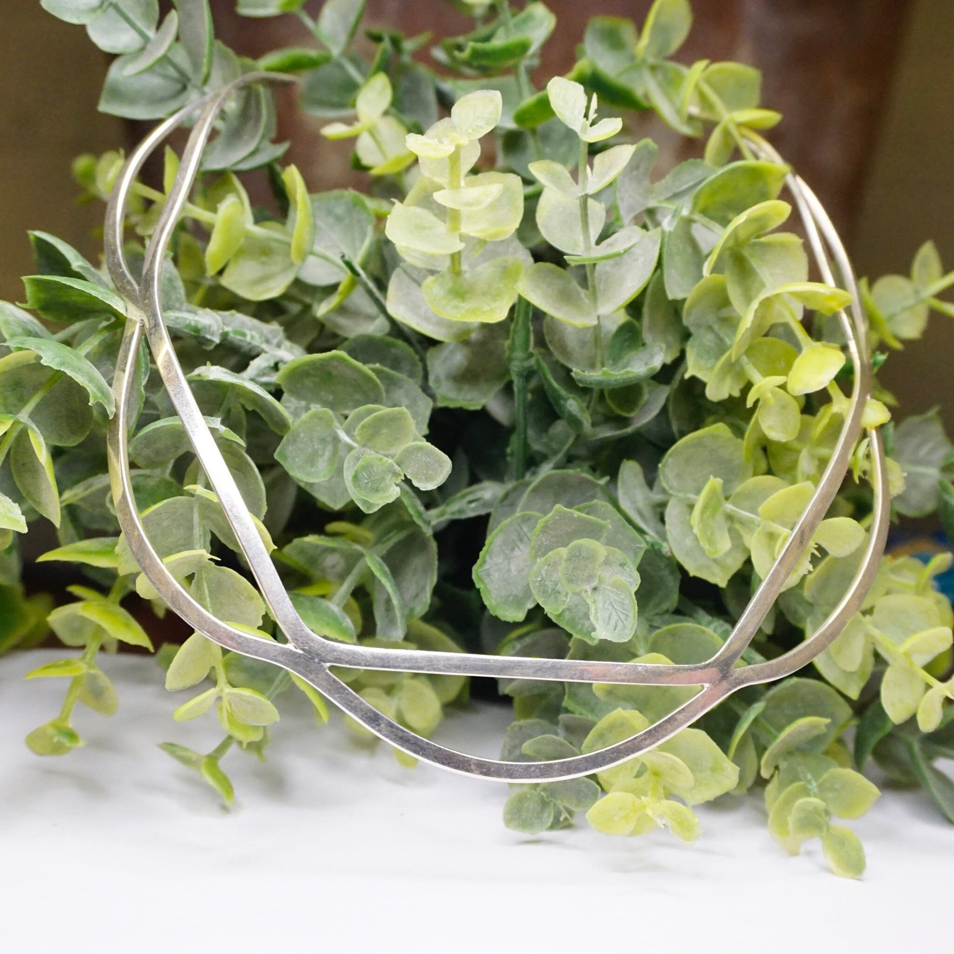 Eucalyptus branches with small round green leaves in a circular metal wreath on a white surface, creating a natural green arrangement.