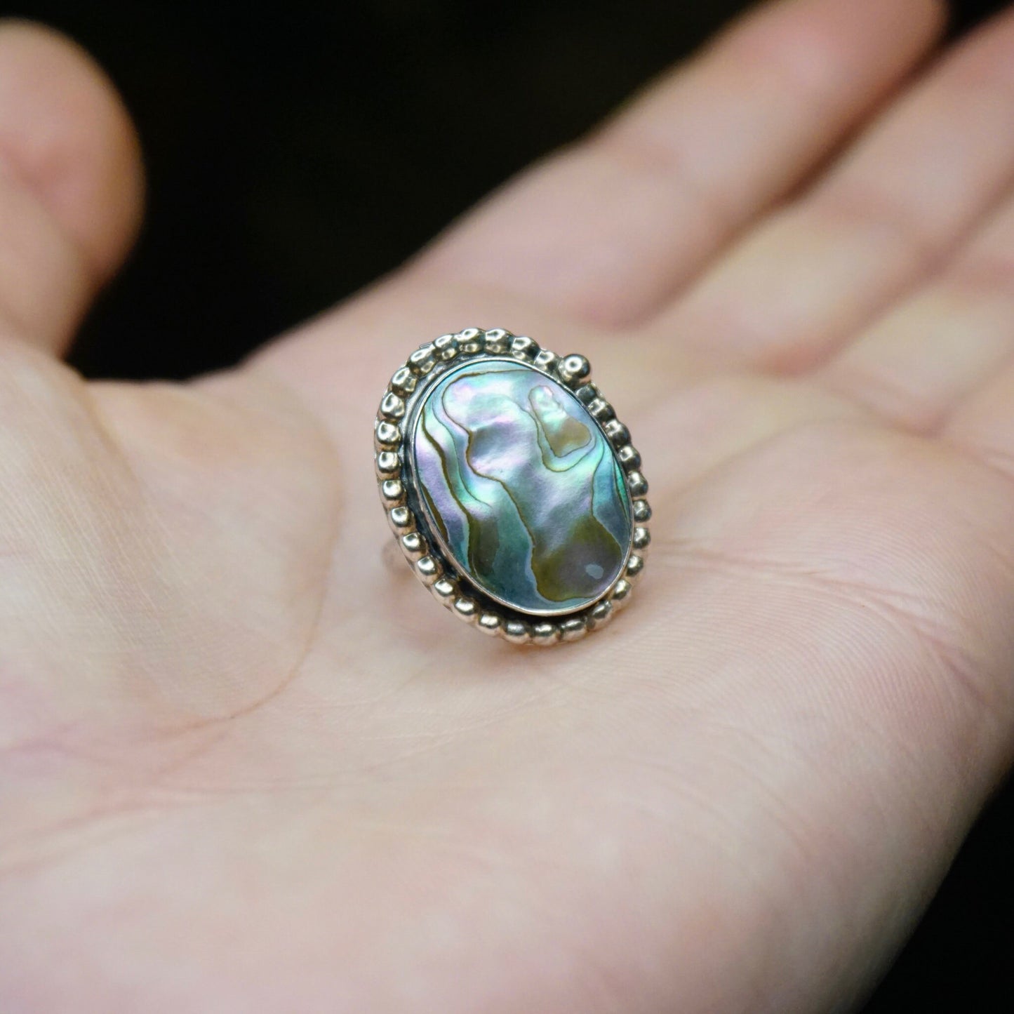 Vintage sterling silver abalone ring with textured design resting on an open palm, showcasing the iridescent abalone shell and intricate silver detailing of the petite hallmarked 925 silver jewelry piece.