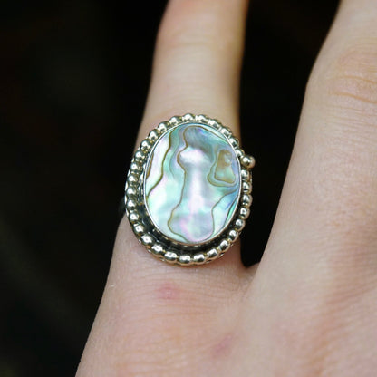 Vintage sterling silver abalone ring with textured design on finger, showcasing iridescent shades of green and blue in the oval abalone shell gemstone surrounded by an ornate silver bezel setting.