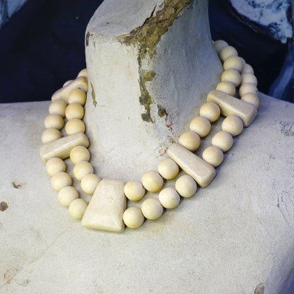 Vintage Gerda Lynggaard Monies two-strand chunky wooden bead necklace with stone accents, shaped in a collar style, resting on a stone surface.