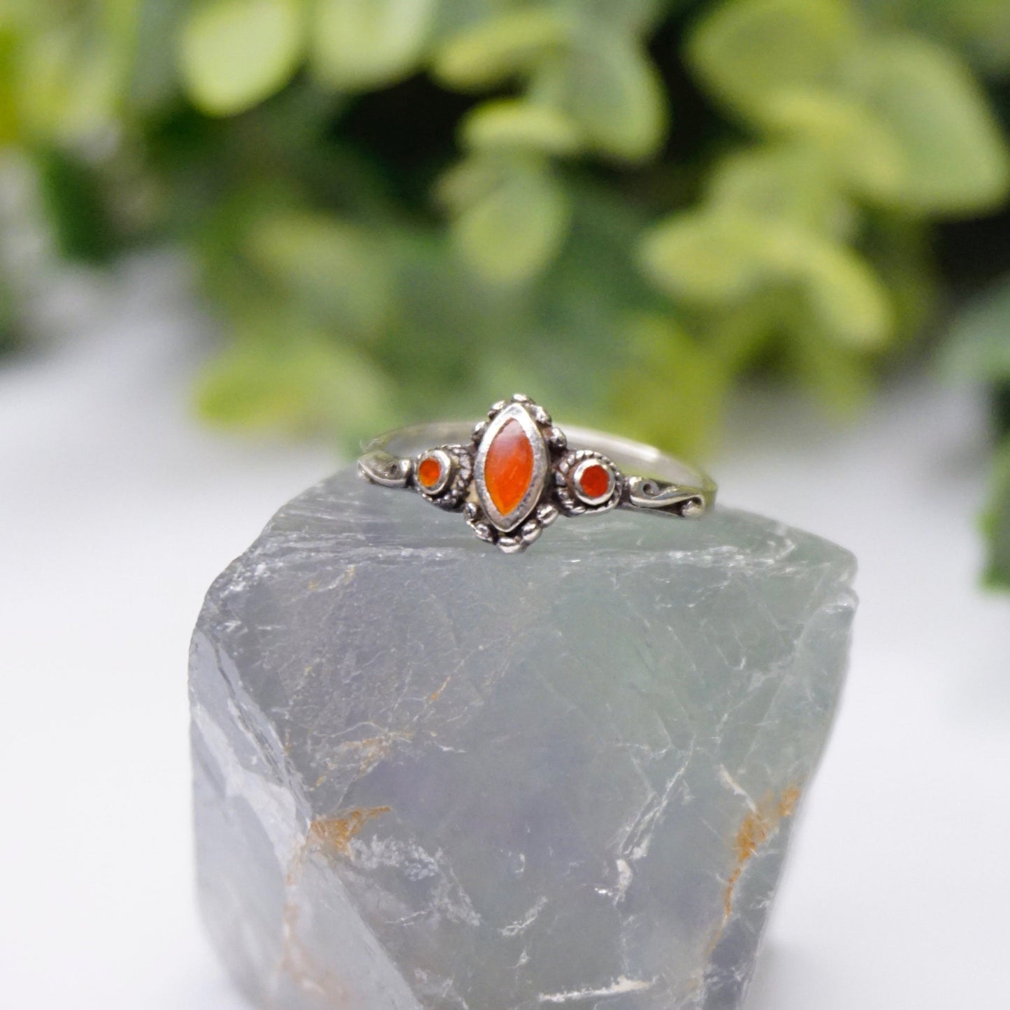 Vintage sterling silver ring with red accent stone and swirl details on natural stone background