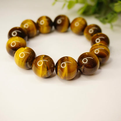 Vintage tigers eye beaded stretch bracelet featuring large, round golden brown tigers eye stones with striated patterns and a glossy polished finish, set against a neutral white background with green foliage.