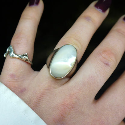 Vintage sterling silver ring with iridescent mother of pearl gemstone on a hand against a black background.