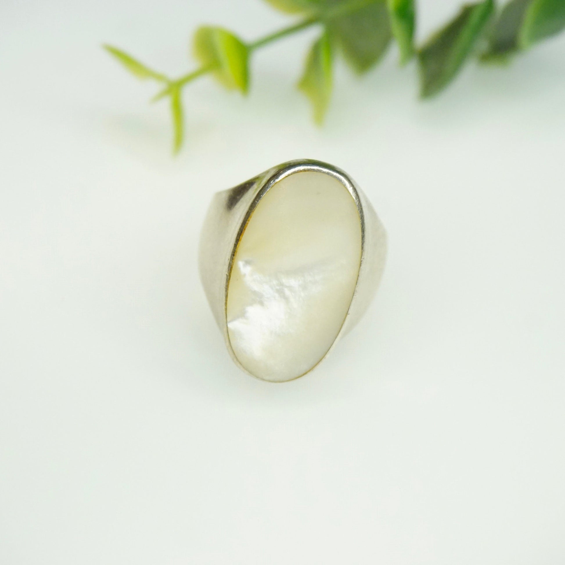 Vintage sterling silver mother of pearl ring on white background with green leaves