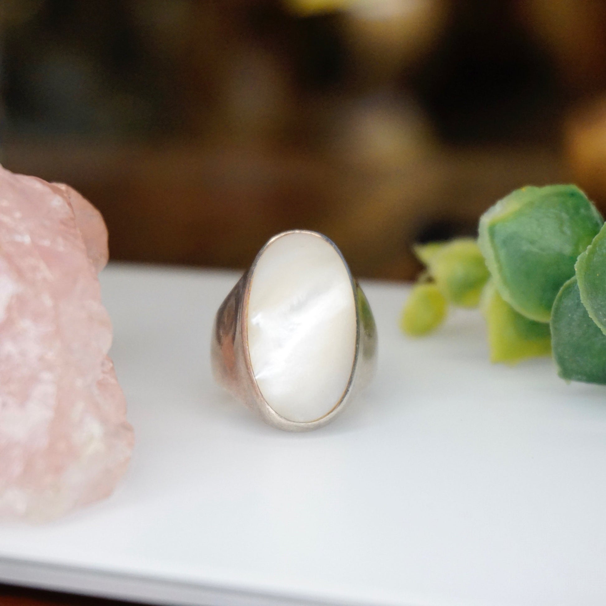 Vintage sterling silver mother of pearl iridescent ring on white surface with pink quartz and green plants in soft focus background