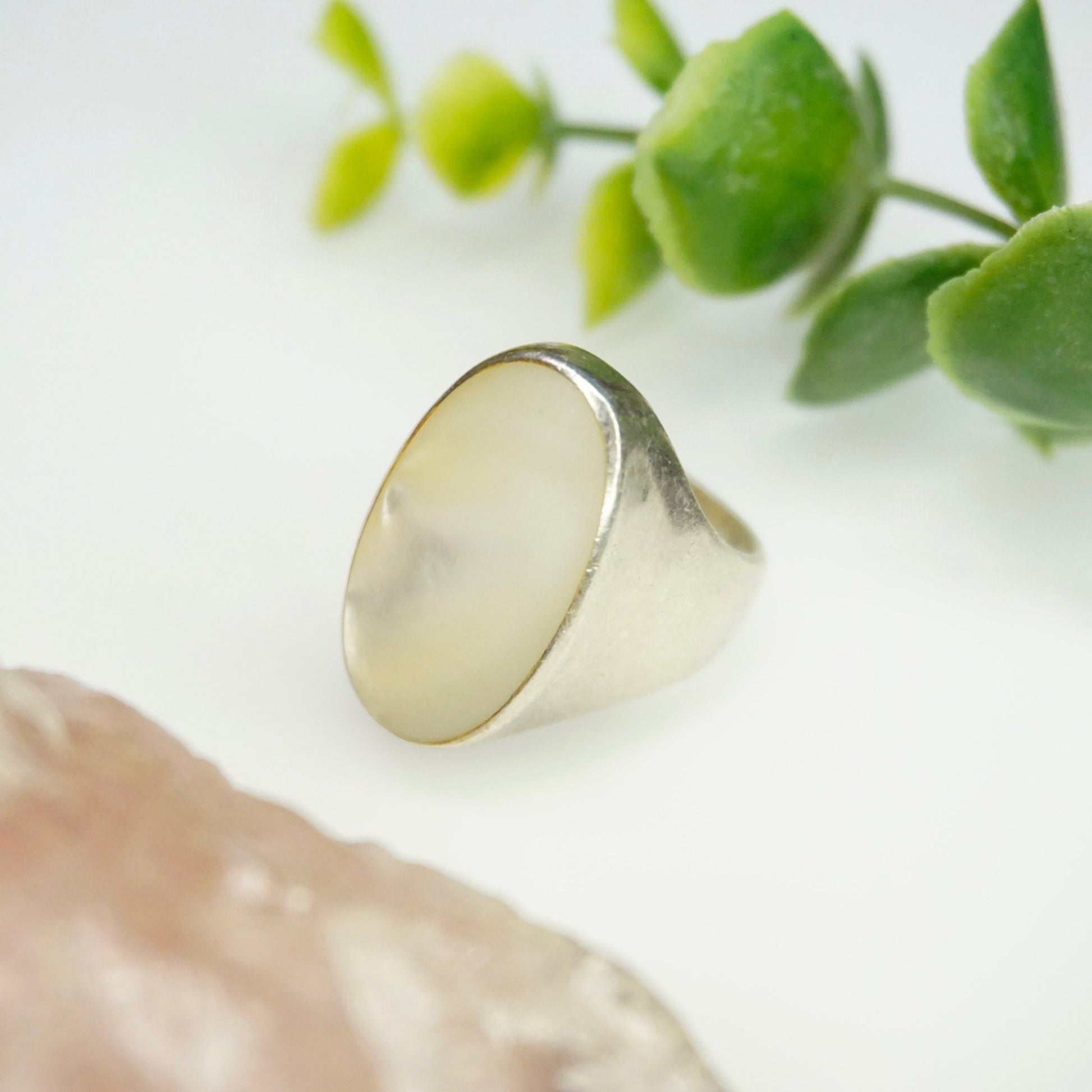 Vintage sterling silver ring with iridescent mother of pearl inlay on white background with green foliage