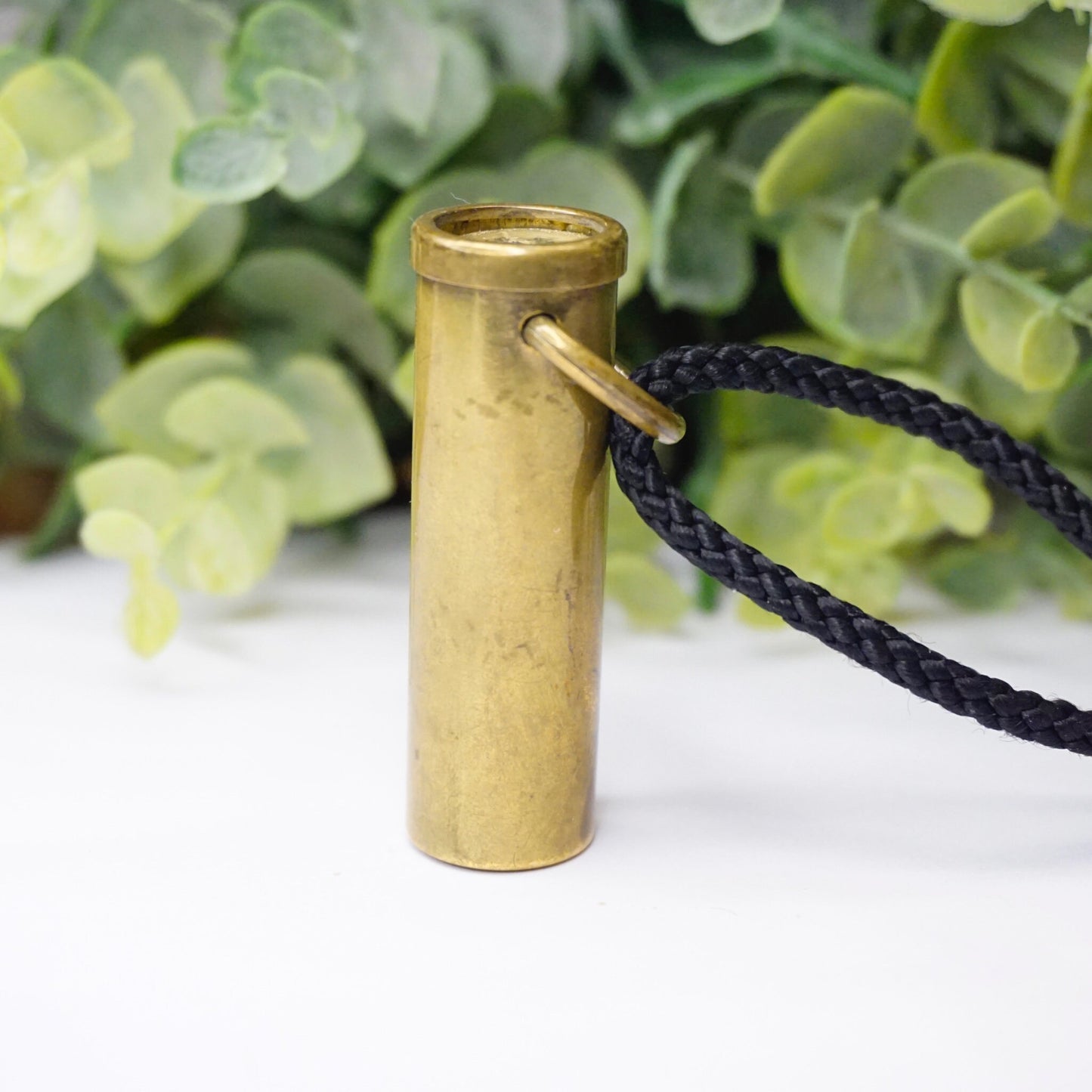 Vintage brass kaleidoscope pendant necklace with black rope, handmade in France, shown in front of green foliage background