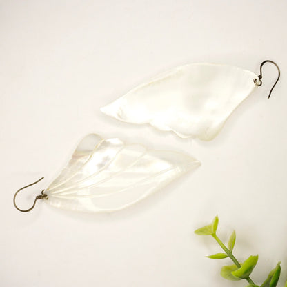 Vintage mother of pearl angel wing earrings on white background with green leaves