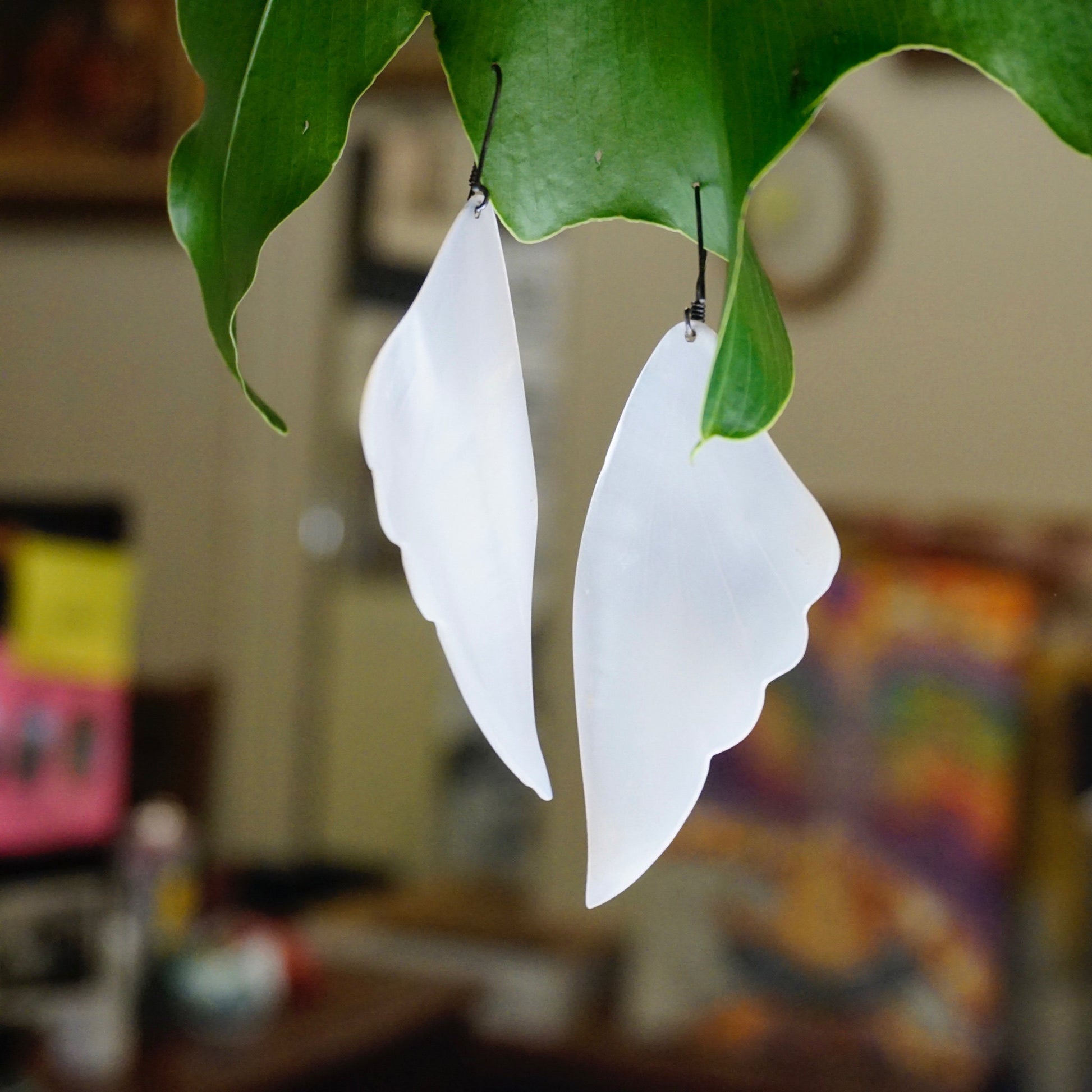 Vintage Mother of Pearl Angel Wing Earrings hanging from green leaves, showcasing their iridescent white shell material and delicate silver dangle design, crafted from 925 sterling silver jewelry.