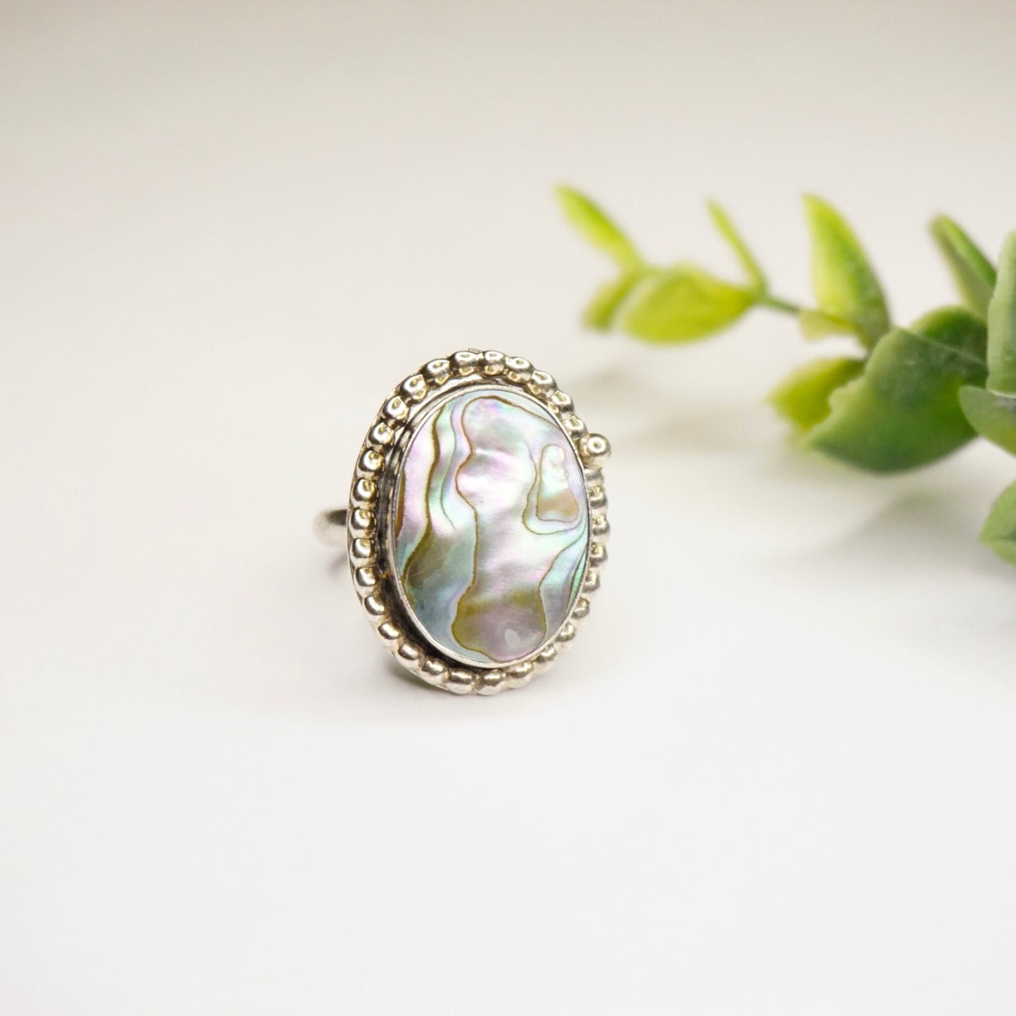 Vintage sterling silver abalone ring with textured bezel setting on white background next to green leaves