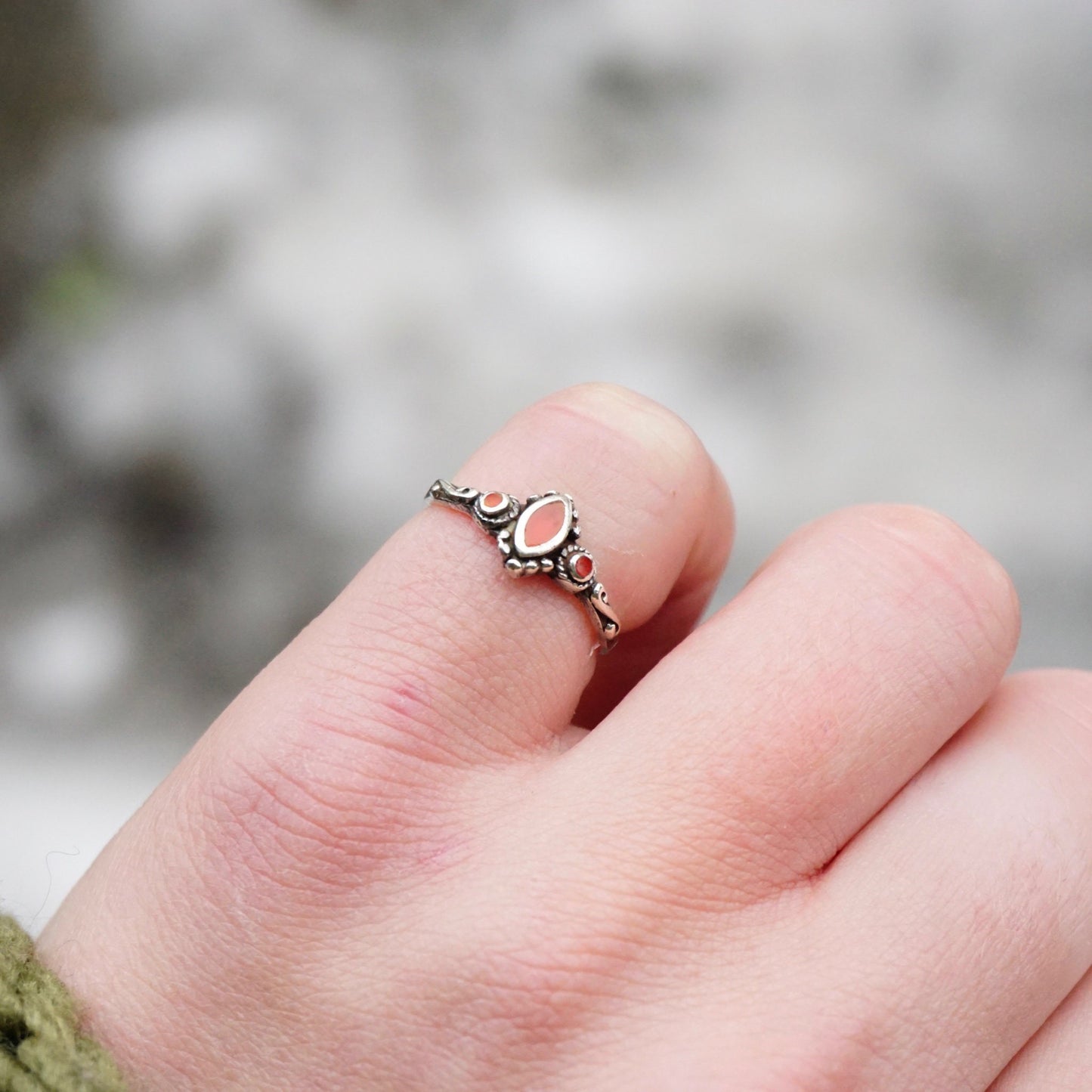 Vintage sterling silver ring with red stone or glass accent on a finger, featuring petite swirl details on the thin band, stamped 925 for sterling silver purity.