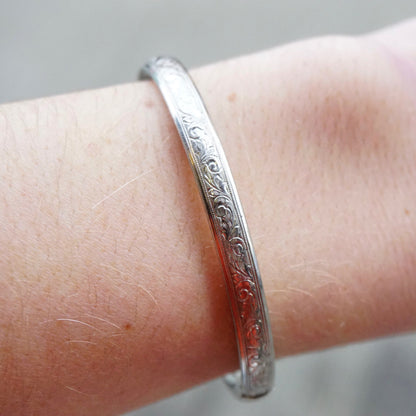 Vintage sterling silver bangle bracelet with intricate engraved scroll pattern and ornate clasp, resting on arm showing detail of the fine metalwork and design.