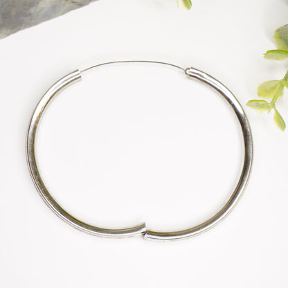 Vintage sterling silver bangle bracelet with scroll clasp and intricate engraved designs, shown on white background with greenery accents.