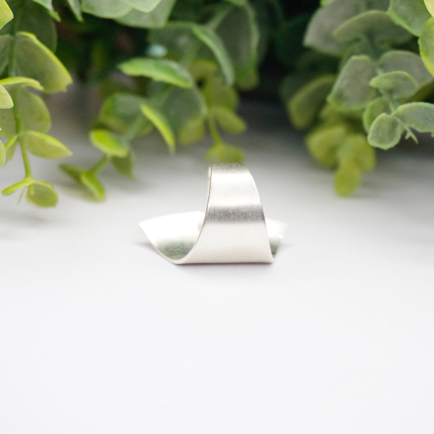 Vintage Kathy Lynn Mayeda sterling silver wrap ring displayed on white surface with green plant in background