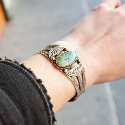 Vintage Native American coin silver cuff bracelet with natural turquoise stone. Intricate handmade silver details adorn the bracelet worn on a wrist. Old pawn jewelry piece showcasing traditional Southwestern craftsmanship.