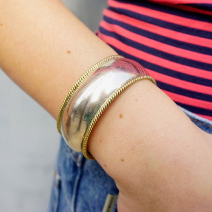 Sterling silver cuff bracelet with gold-tone woven trim on an arm against a red and navy blue striped shirt.