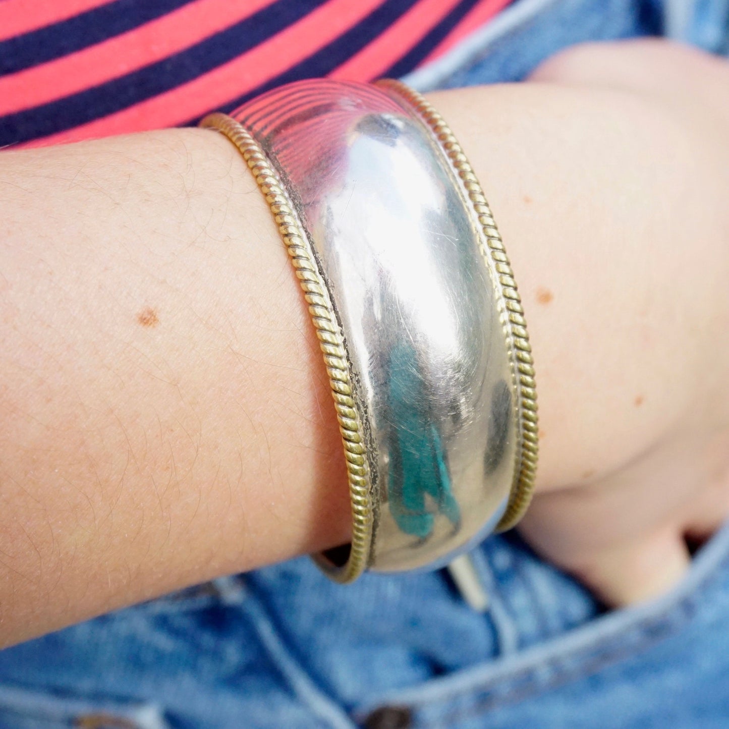 Vintage sterling silver cuff bracelet with gold tone accents and woven brass trim, worn on a woman's wrist against denim jeans and a striped shirt.