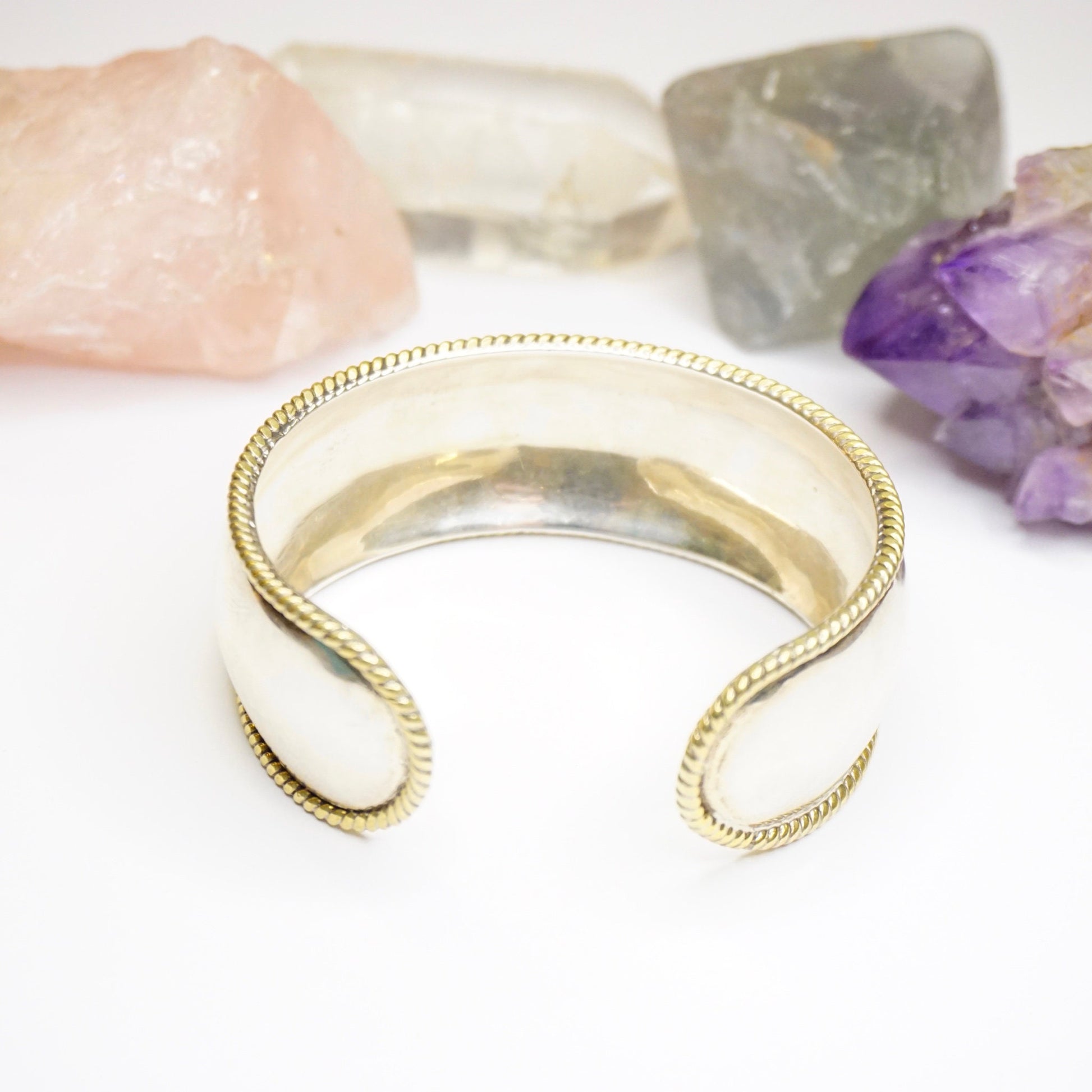 Vintage sterling silver cuff bracelet with woven gold tone brass trim accents from Taxco, Mexico. Minimalist 925 silver bracelet with open ends on white background with amethyst stones.