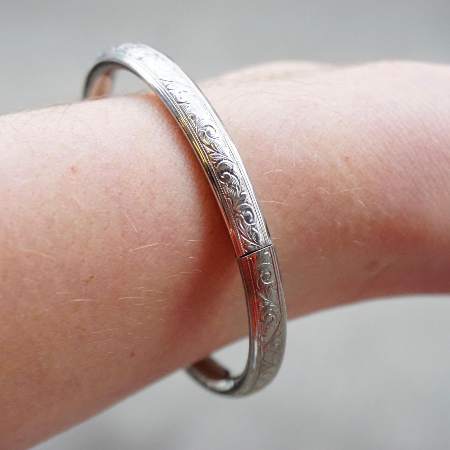 Sterling silver bangle bracelet with engraved scrollwork design and clasp, shown on wrist