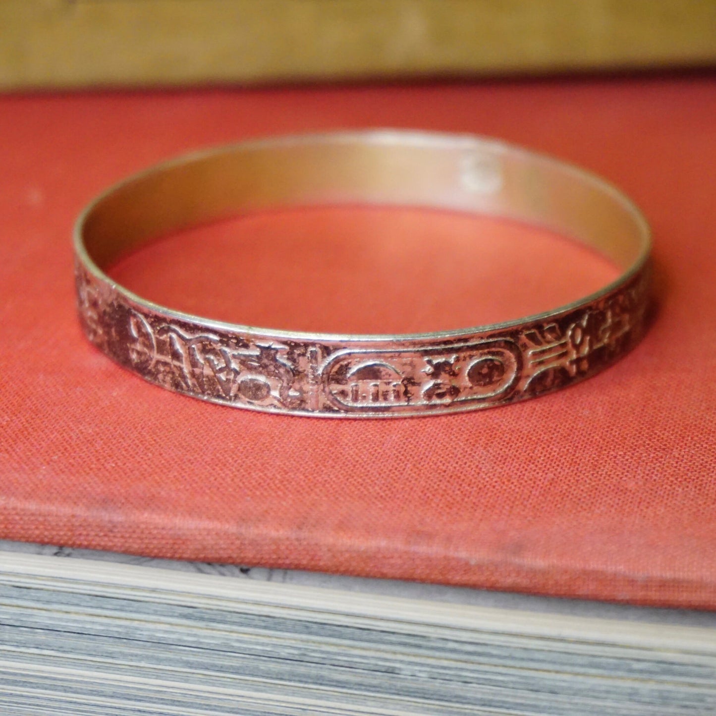 Vintage TAXCO 925 sterling silver bangle bracelet with hieroglyphic Egyptian motif design, made in Mexico, displayed on red cloth-covered book.