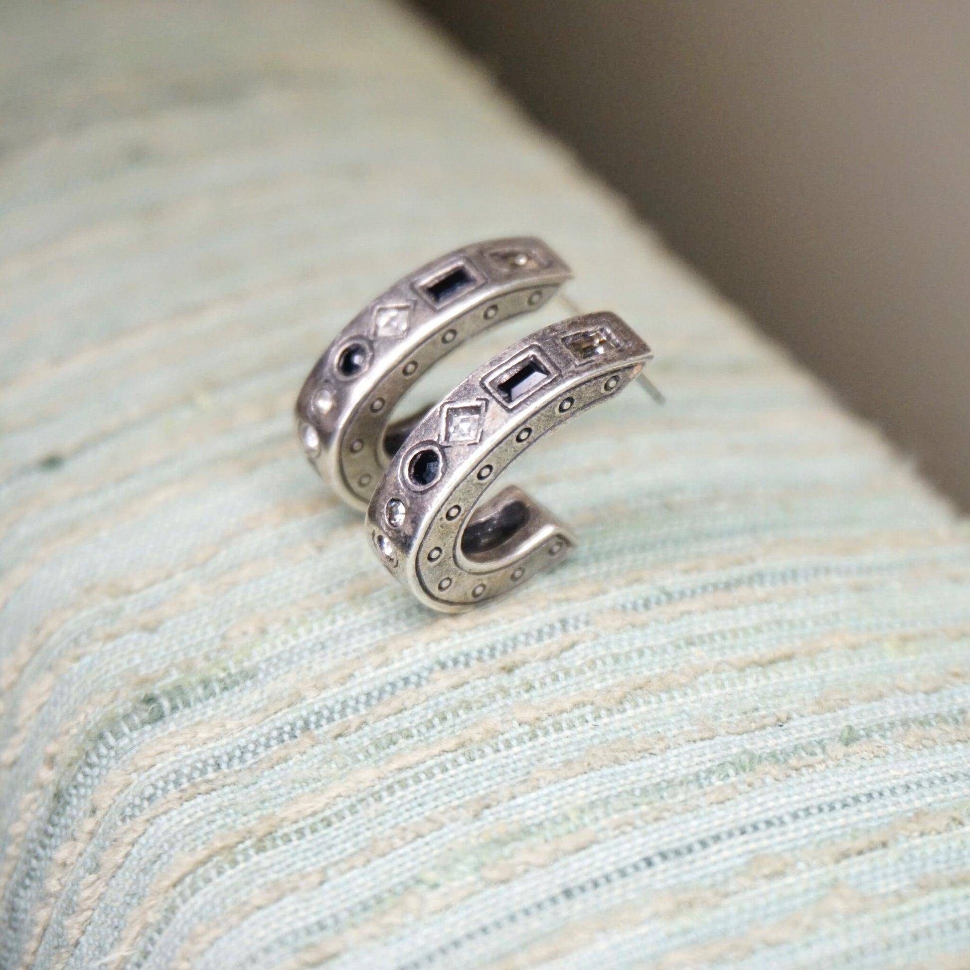 Vintage silver-plated half moon stud earrings with black and white crystals in a modernist style, resting on ribbed light blue fabric.