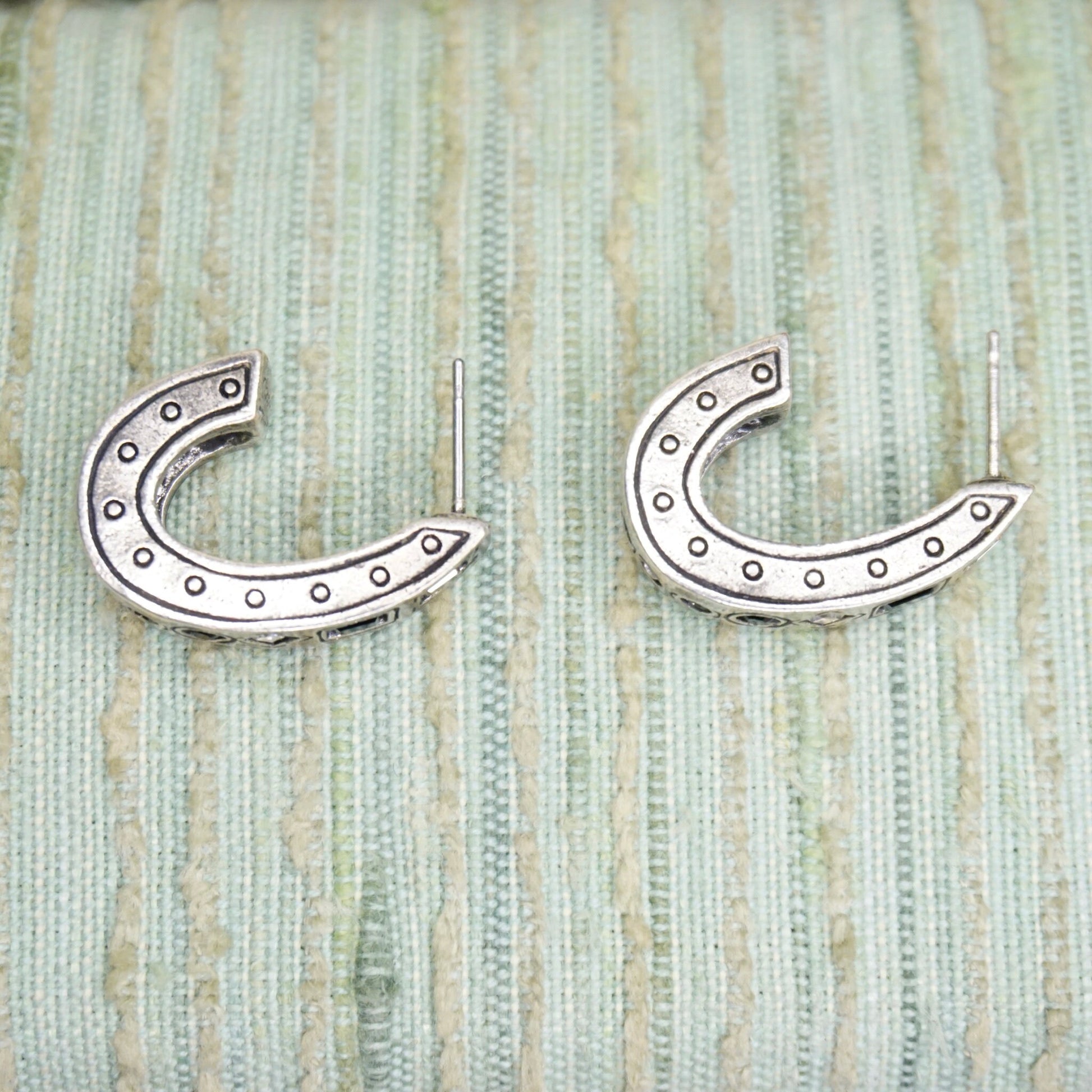 Vintage silver plated half moon stud earrings with decorative rivet details, displayed on textured sage green fabric background.