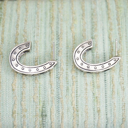 Vintage silver plated half moon stud earrings with decorative rivet details, displayed on textured sage green fabric background.