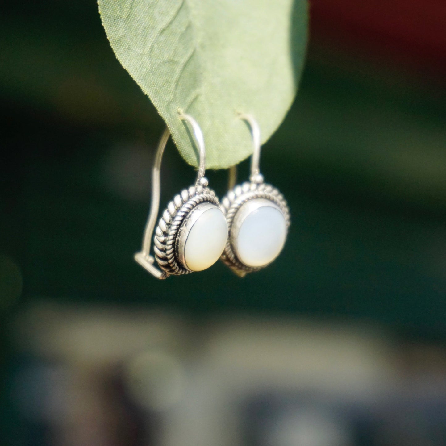 Vintage moonstone and silver drop earrings on green leaf, shallow focus