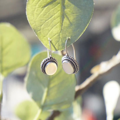 Vintage moonstone and silver drop earrings on locking kidney ear wires, shown hanging from a green leaf outdoors.