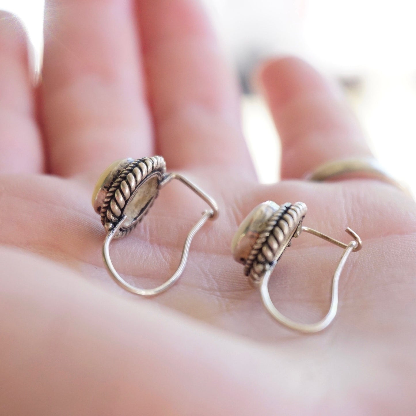 Vintage moonstone and silver drop earrings on open hand, featuring intricate silver leaf design and petite moonstone cabochons hung from locking kidney hook ear wires.