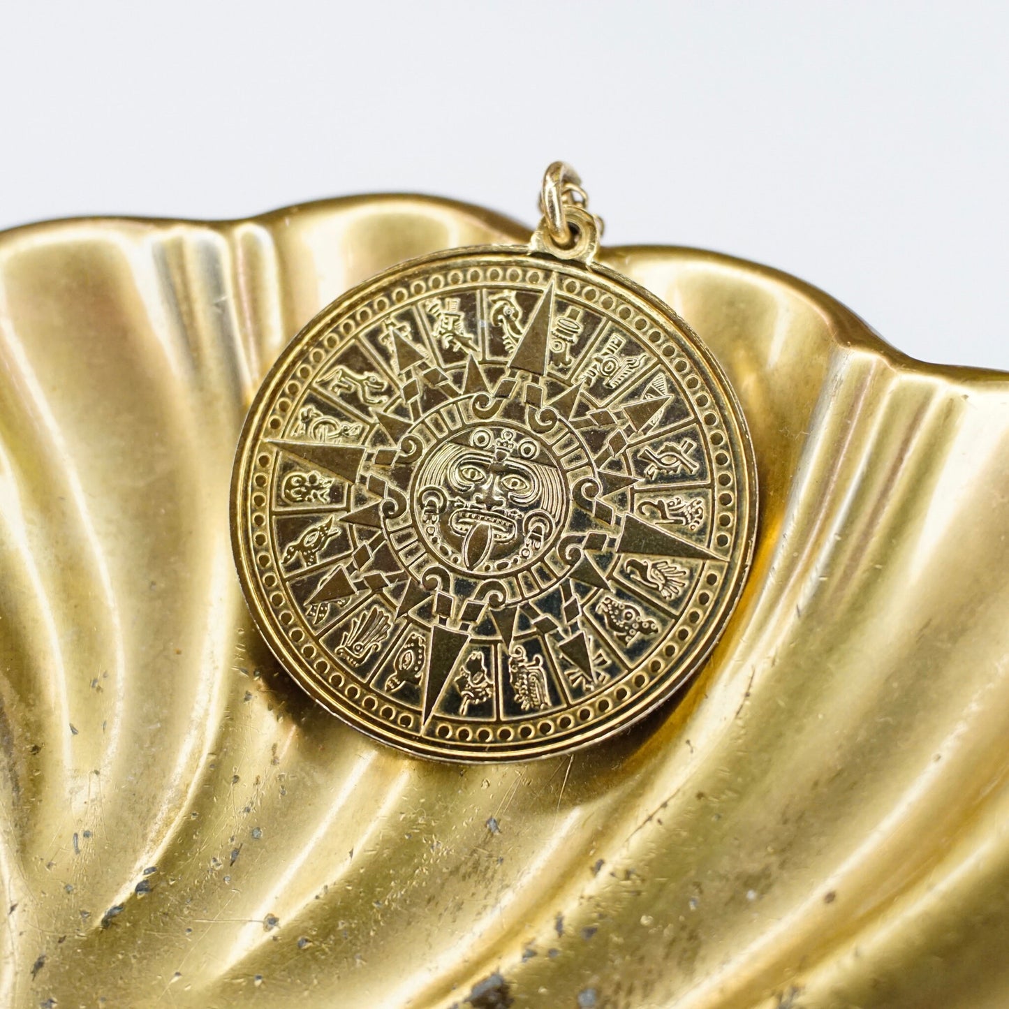 Vintage gold Mayan sun calendar pendant necklace with intricate Aztec carvings and designs on a textured gold background