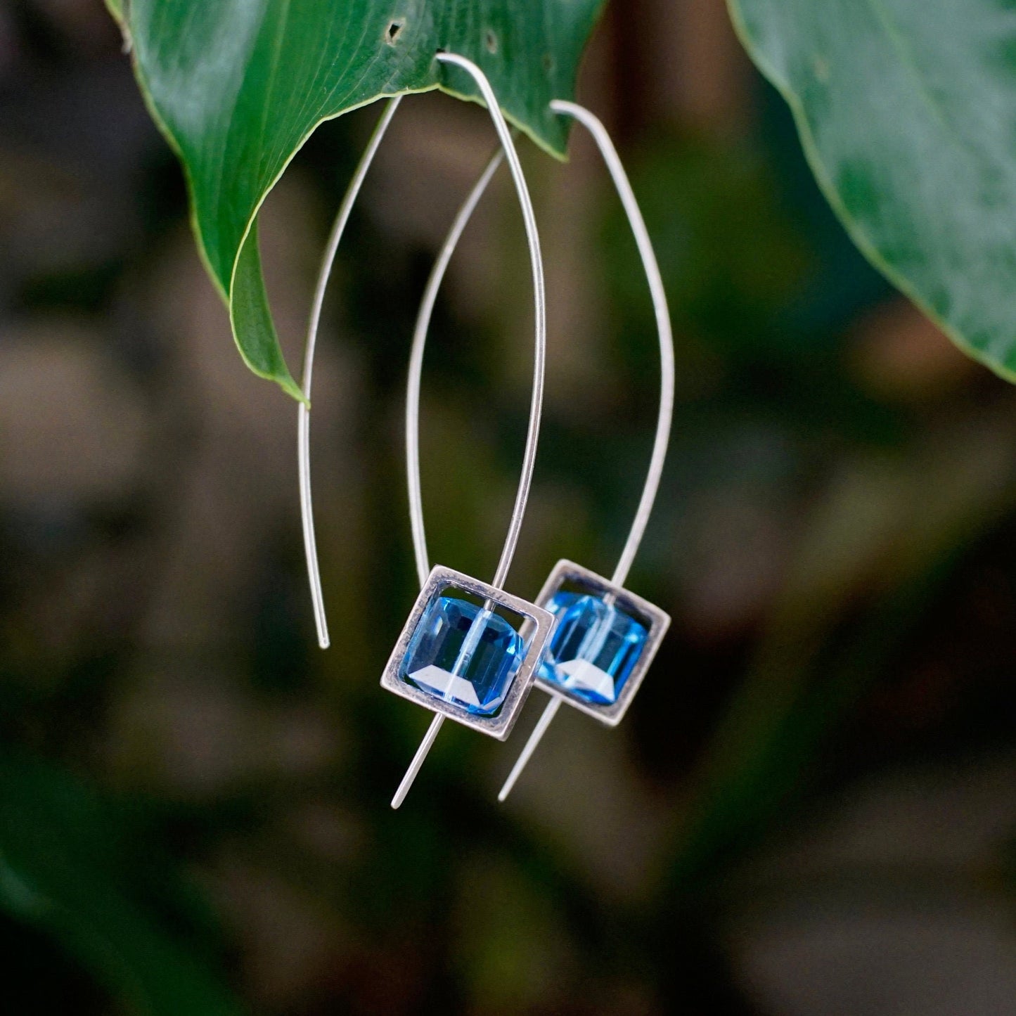 Vintage sterling silver marquise hook earrings with framed blue glass stones hanging from green leaves, creating a minimalist and elegant look.