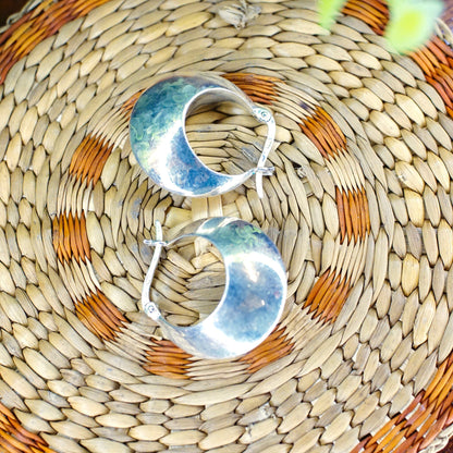 Vintage sterling silver half moon hoop earrings on woven rattan surface