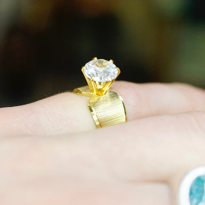 Vintage gold tone solitaire ring with round cut cubic zirconia stone in 6-prong setting displayed on hand, size 5 US.