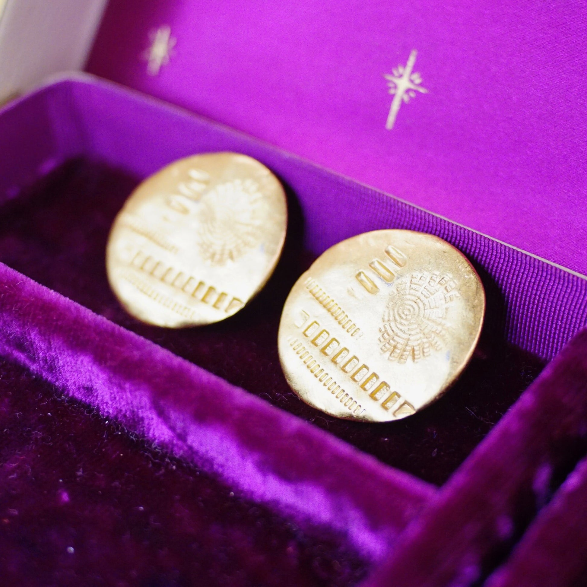 Vintage gold tone disc stud earrings with hammered and stamped abstract details, displayed in a purple velvet jewelry box.