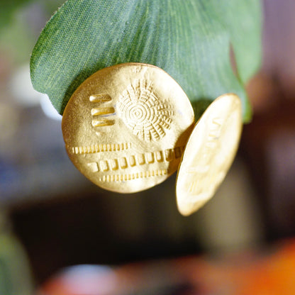 Vintage gold tone disc stud earrings with abstract round hammered and stamped details, unique artisan post earrings jewelry closeup on green leaf