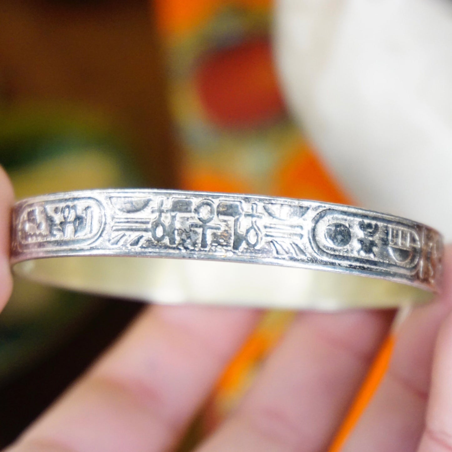 Vintage TAXCO Sterling Silver Hieroglyphic Bangle Bracelet with Egyptian motifs, made in Mexico 925 silver, held in hand against colorful fabric background