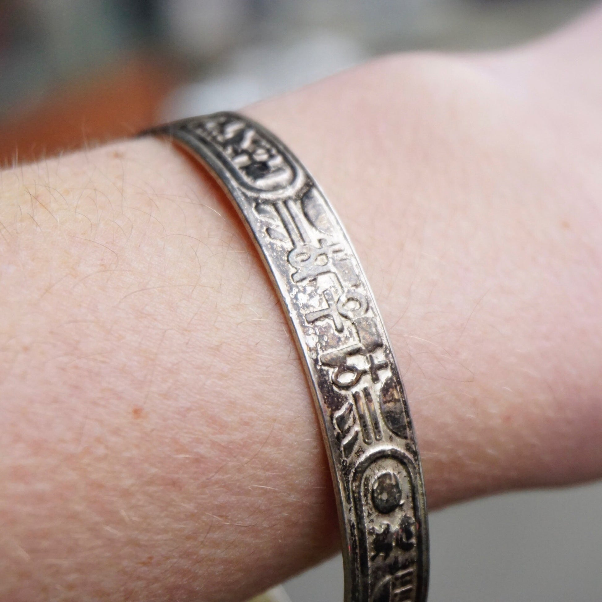 Vintage TAXCO sterling silver bangle bracelet with Egyptian hieroglyphic motifs, made in Mexico 925 silver jewelry, shown on wrist against blurred background.