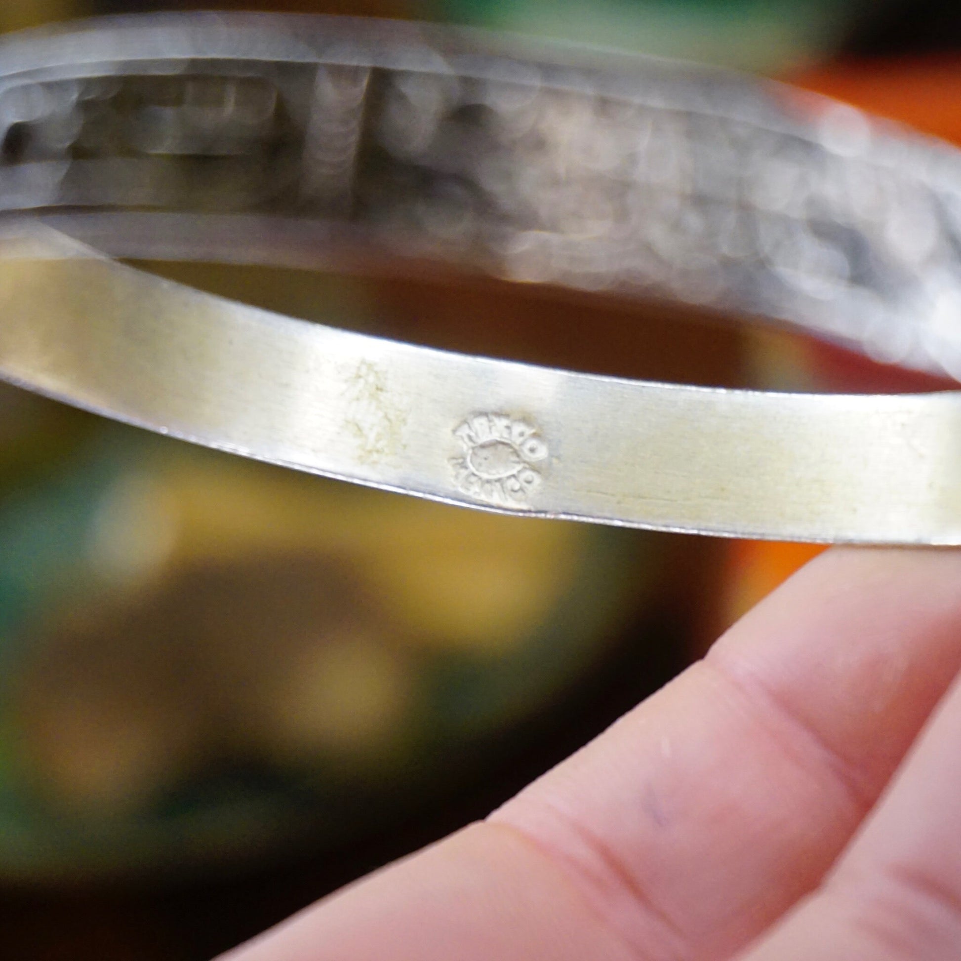 Vintage Taxco sterling silver bangle bracelet with Egyptian hieroglyphic motifs, made in Mexico 925 silver, held in hand to show engraved details on the inside of the bracelet.