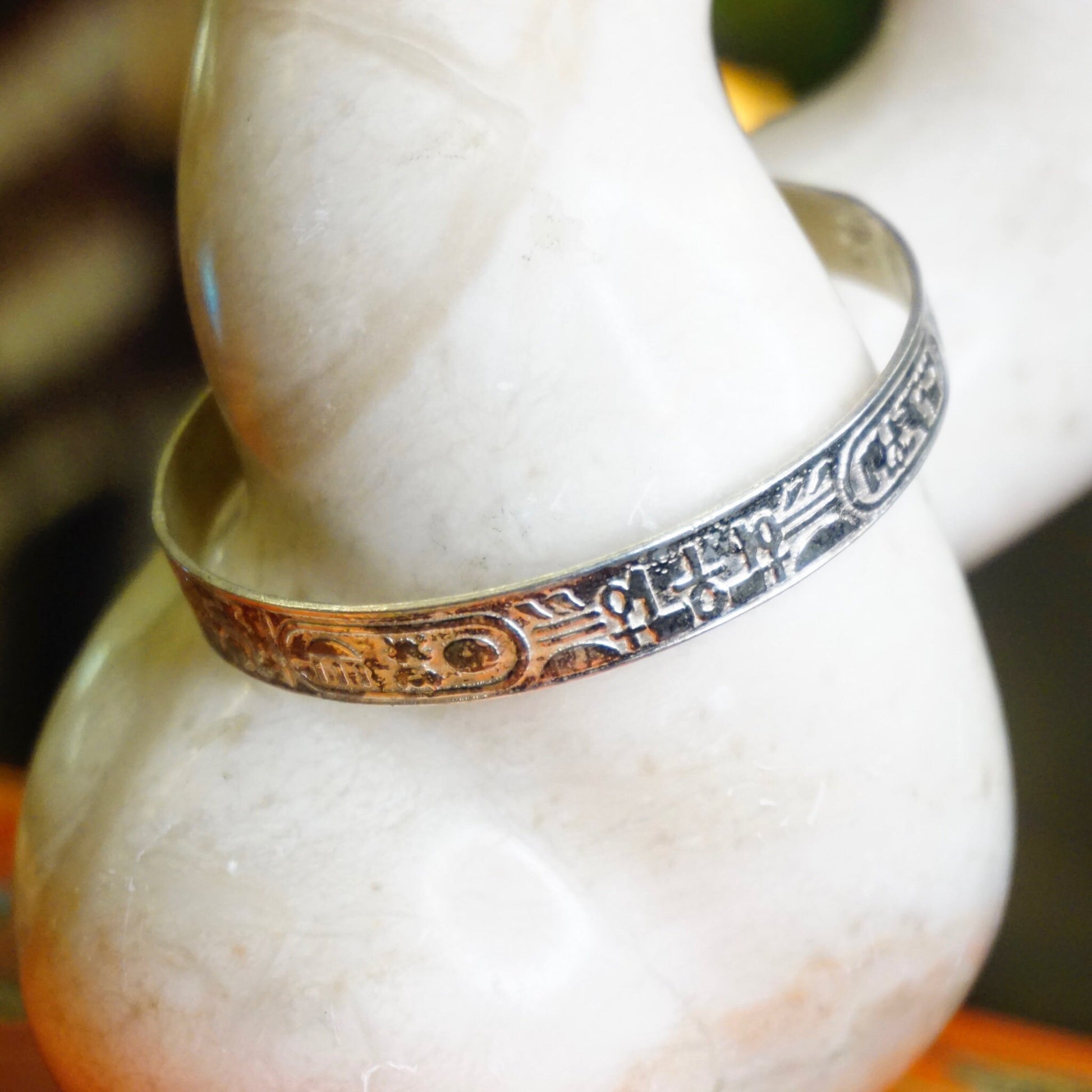 Vintage TAXCO Sterling Silver Hieroglyphic Bangle Bracelet with Egyptian motifs, made in Mexico 925 silver, shown on a white decorative object.