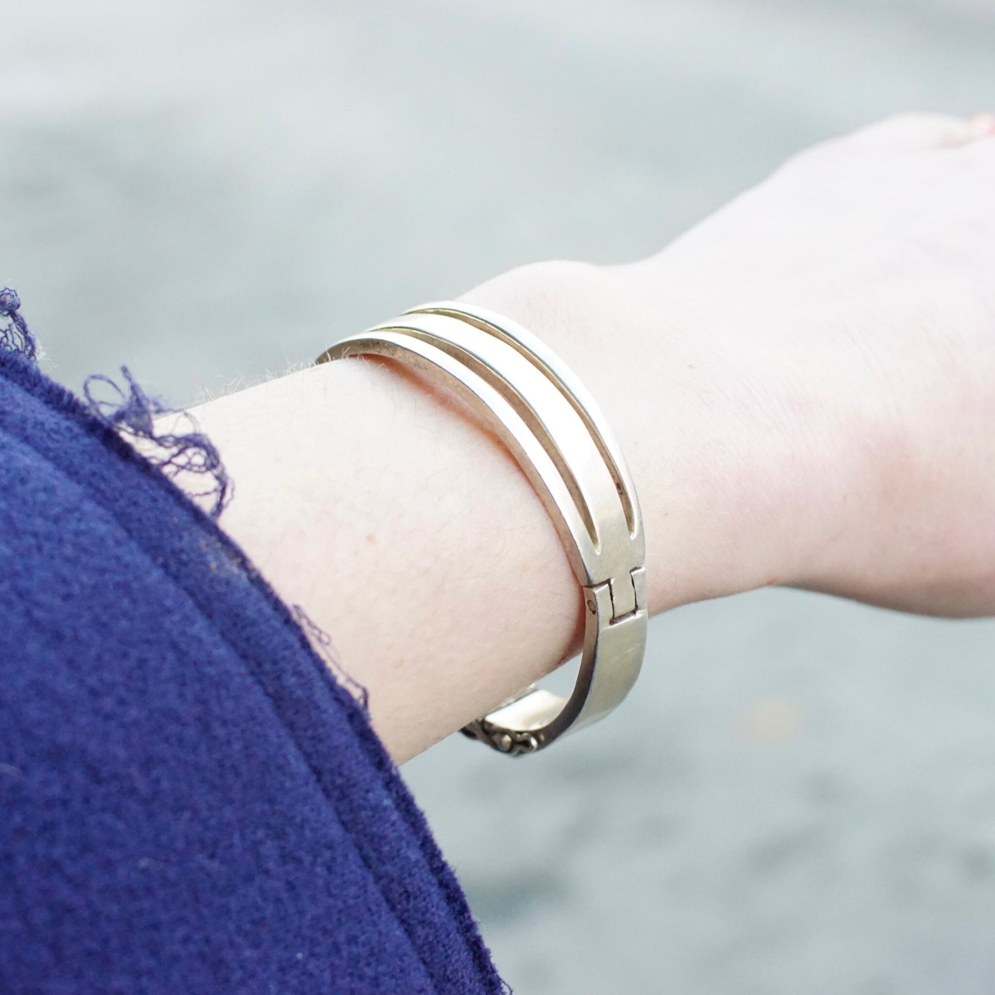 Vintage sterling silver hinged bangle bracelet with cut out design from Taxco, Mexico, worn on a model's wrist against a light blue background.