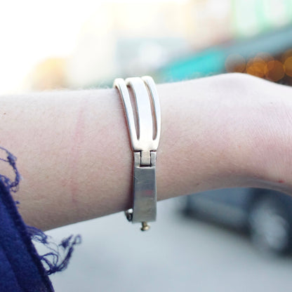 Vintage sterling silver hinged bangle bracelet with cut out modernist design from Taxco, Mexico, shown on a person's wrist against a blurred background.