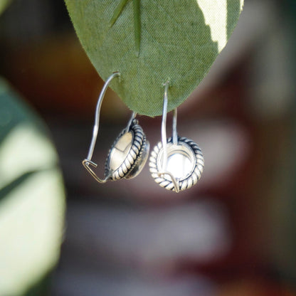 Vintage moonstone and silver drop earrings hanging from green leaf, showing intricate wreath design on silver bezel surrounding the glowing moonstone cabochons, suspended from silver kidney ear wires.