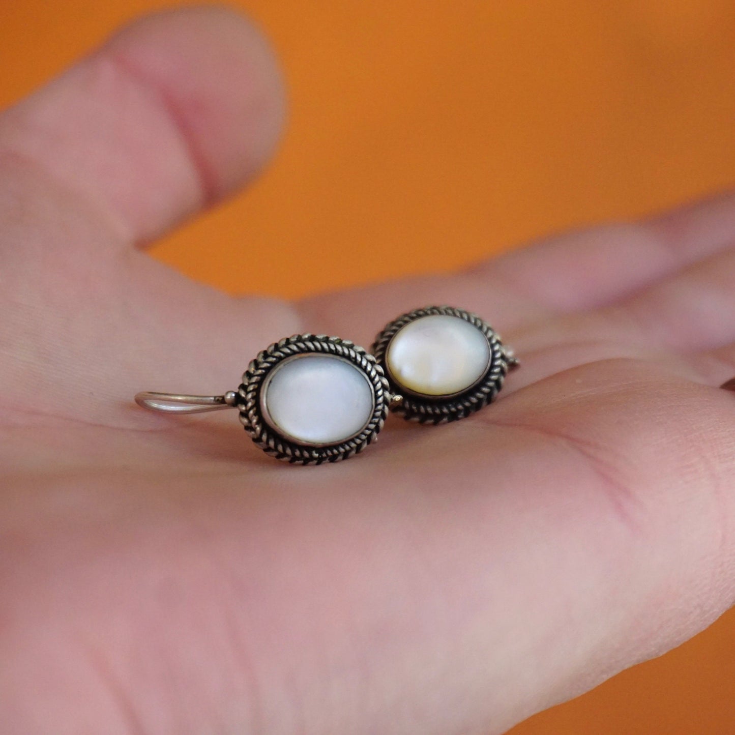 Vintage moonstone and silver drop earrings on an open hand, featuring petite oval moonstone cabochons set in ornate silver bezels with locking kidney ear wire closures.